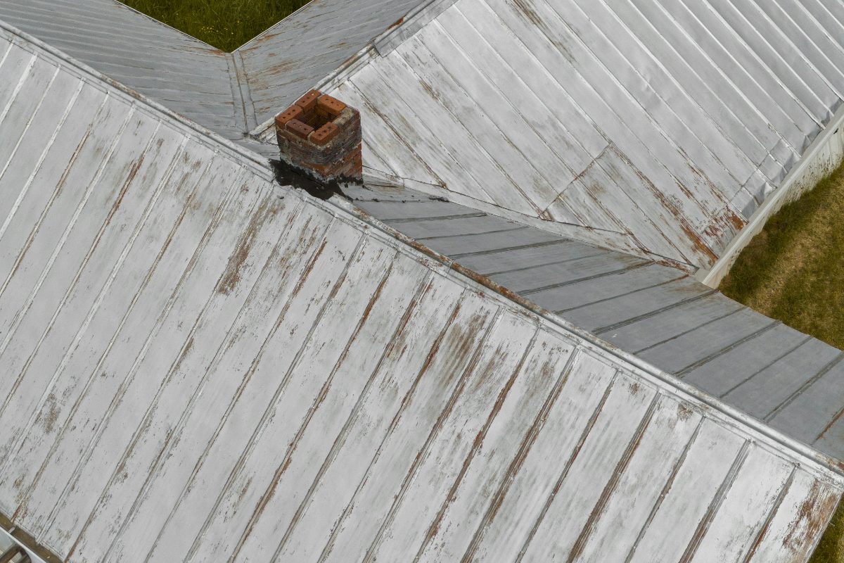 Aerial drone inspection of a weathered metal roof with damaged chimney flashing
